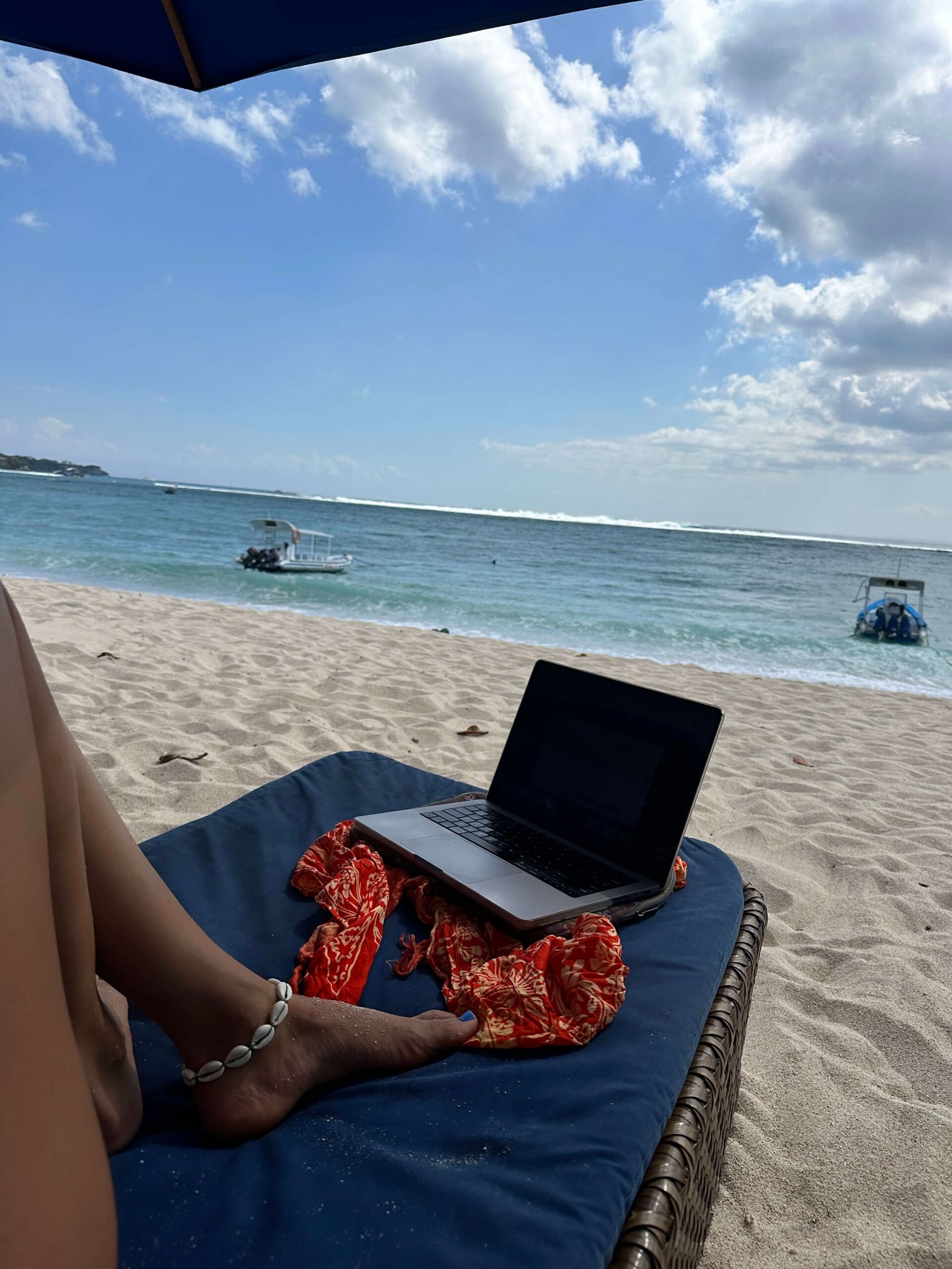 Eine Frau arbeitet mit ihrem Laptop an ihrem Online Business am Strand.